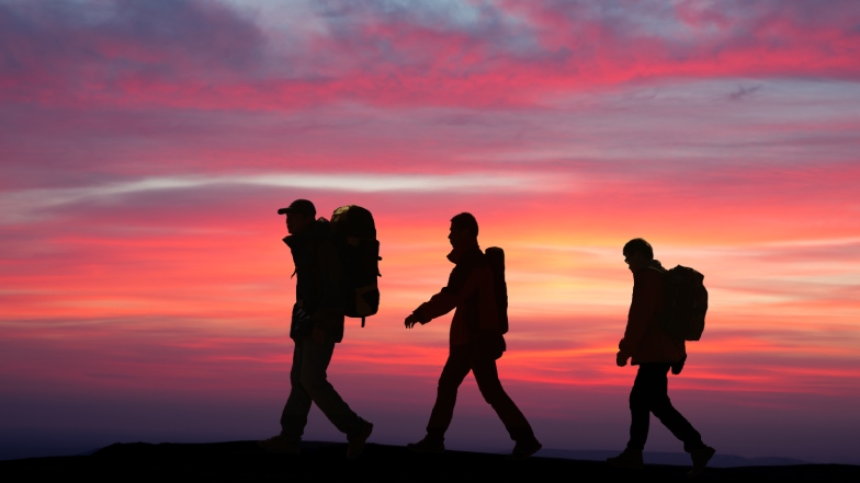 Silhouettes of three hikers walking at sunset