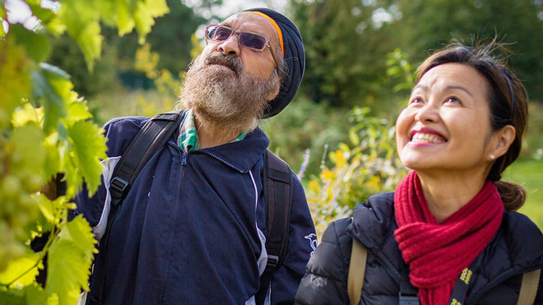 A My Guide volunteer helps a Sikh man to use a cane and navigate gardens