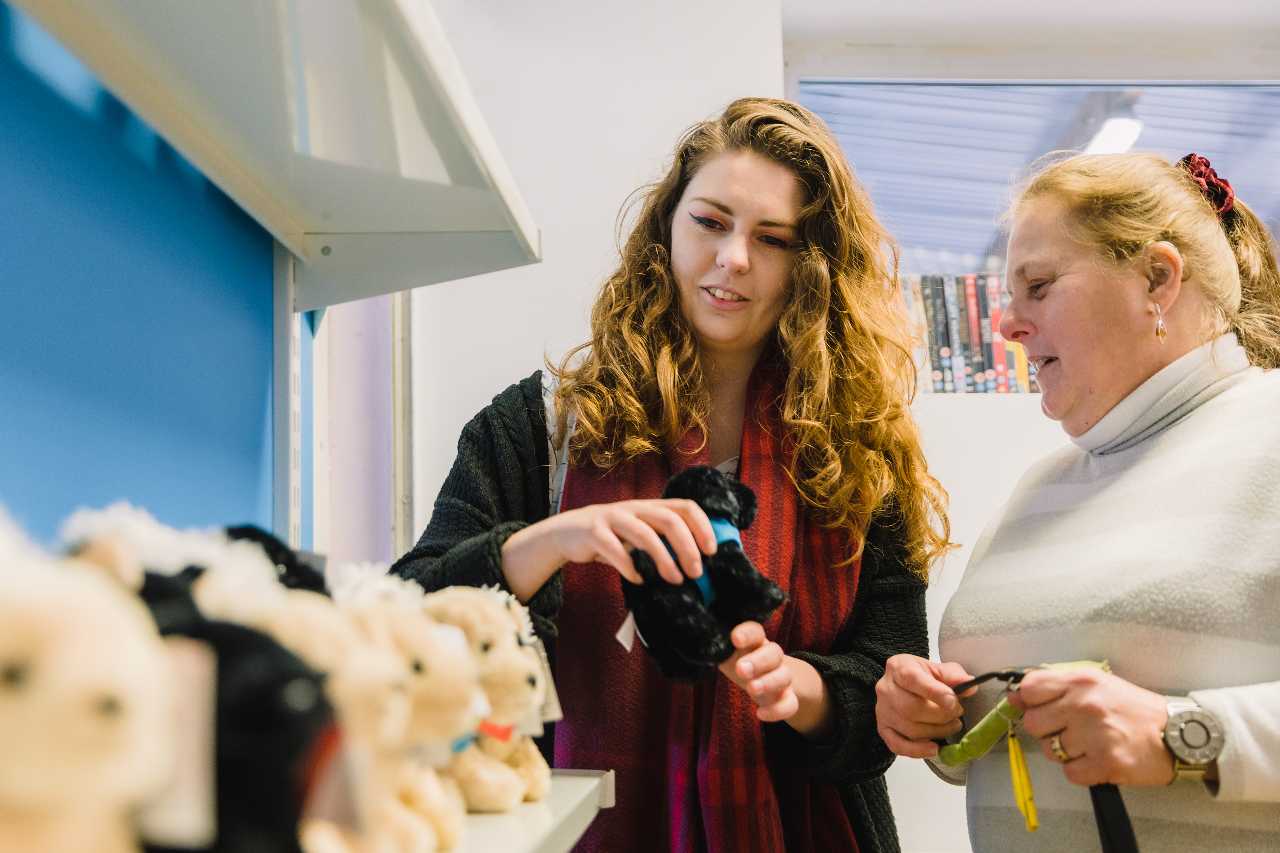 Young woman showing dog stuffed toys to a VI woman