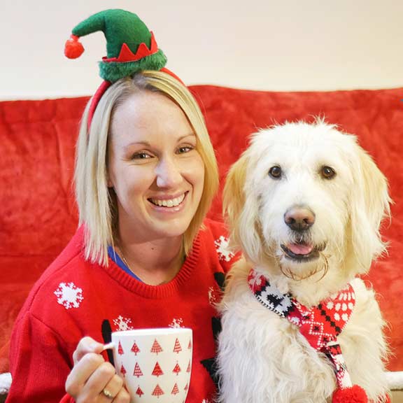 Woman with festive hat and jumper sitting next to a Guide Dog wearing a scarf