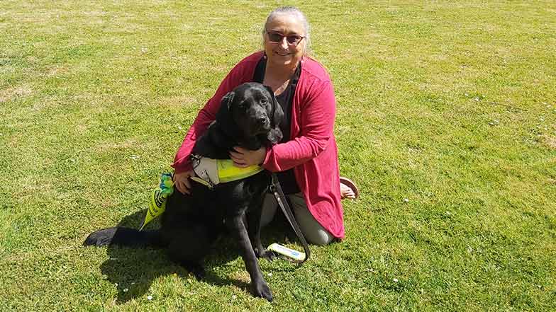 Guide dog owner sitting with her guide dog on grass