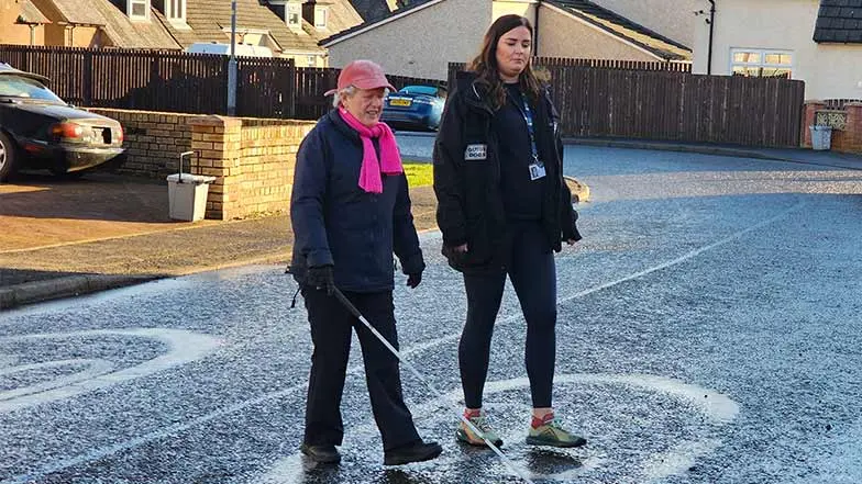 Margaret walks with a long cane alongside her Visual Rehabilitation Specialist.