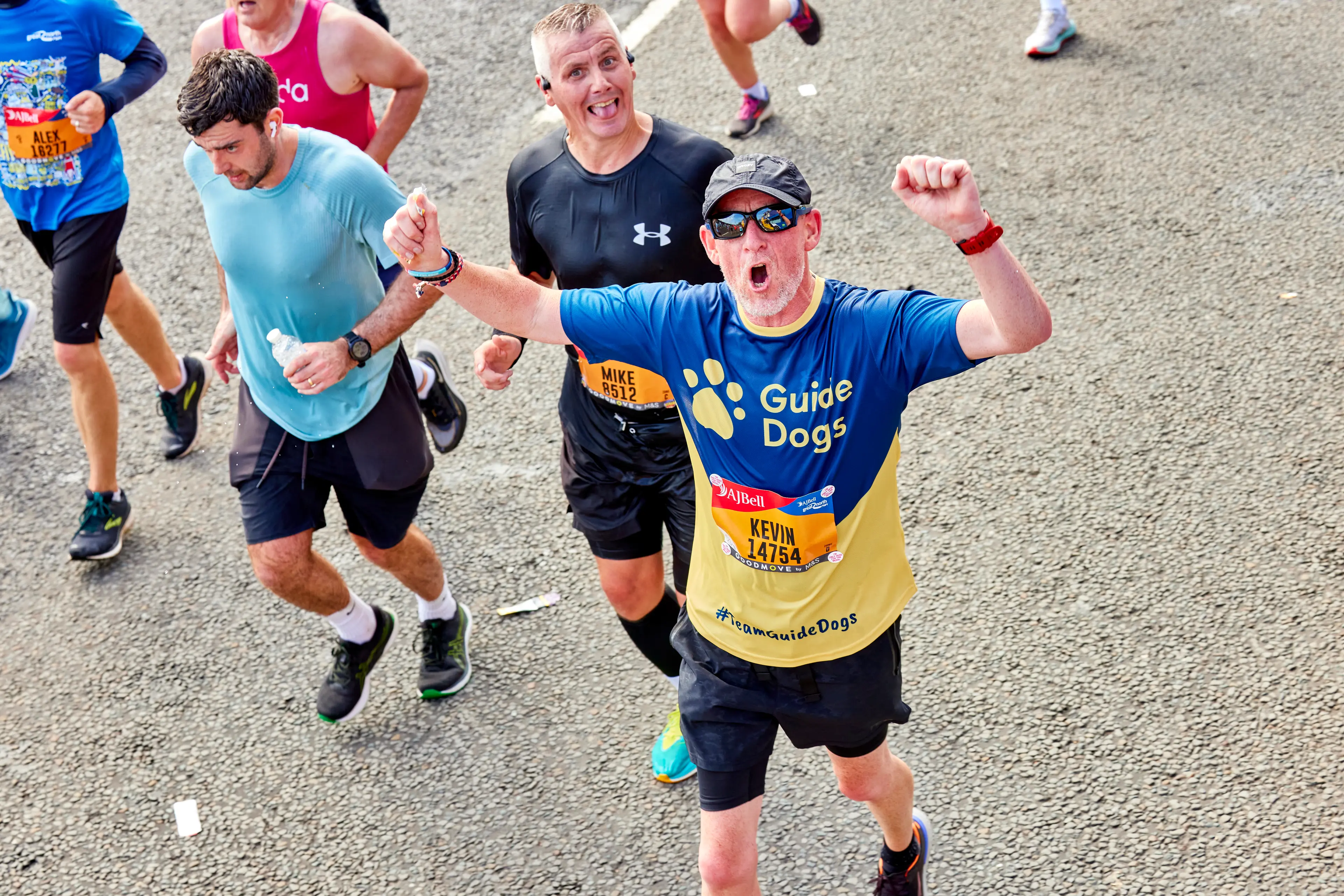 A runner for Guide Dogs waves his hand in the air as he passes cheering supporters.