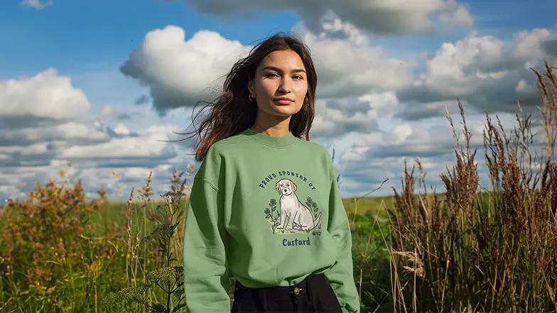 Woman in the countryside wearing a sweatshirt with sponsored pup Custard design.
