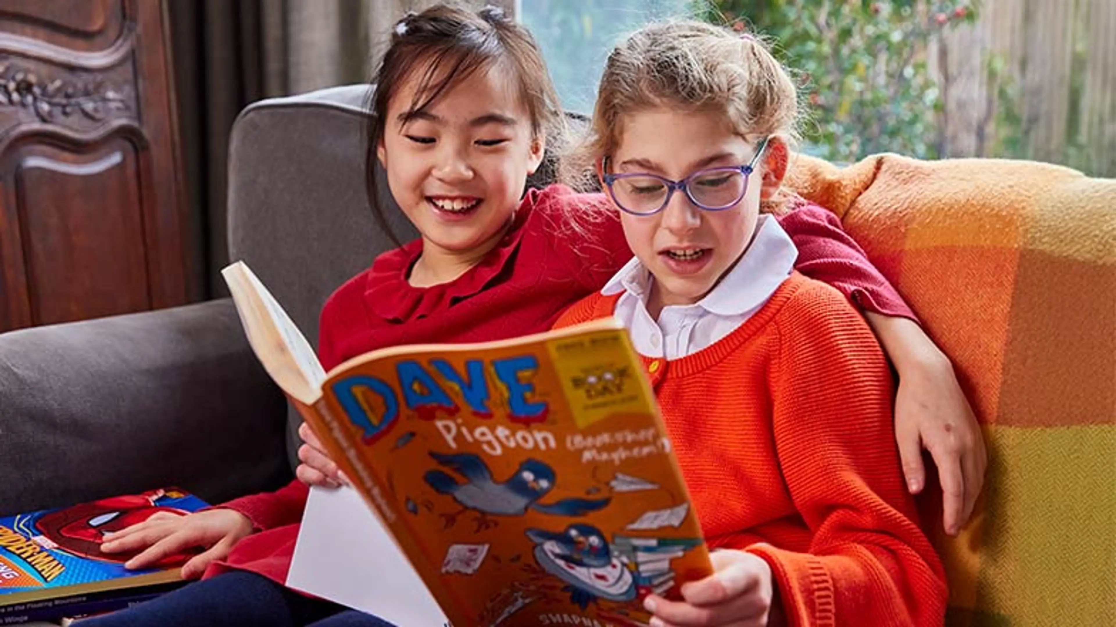 2 girls, huddled together on a sofa, enjoying a large-print book.