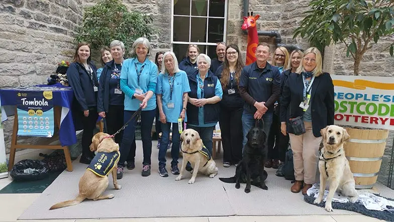 Guide Dogs staff and dogs in training with postcode lottery staff and posters