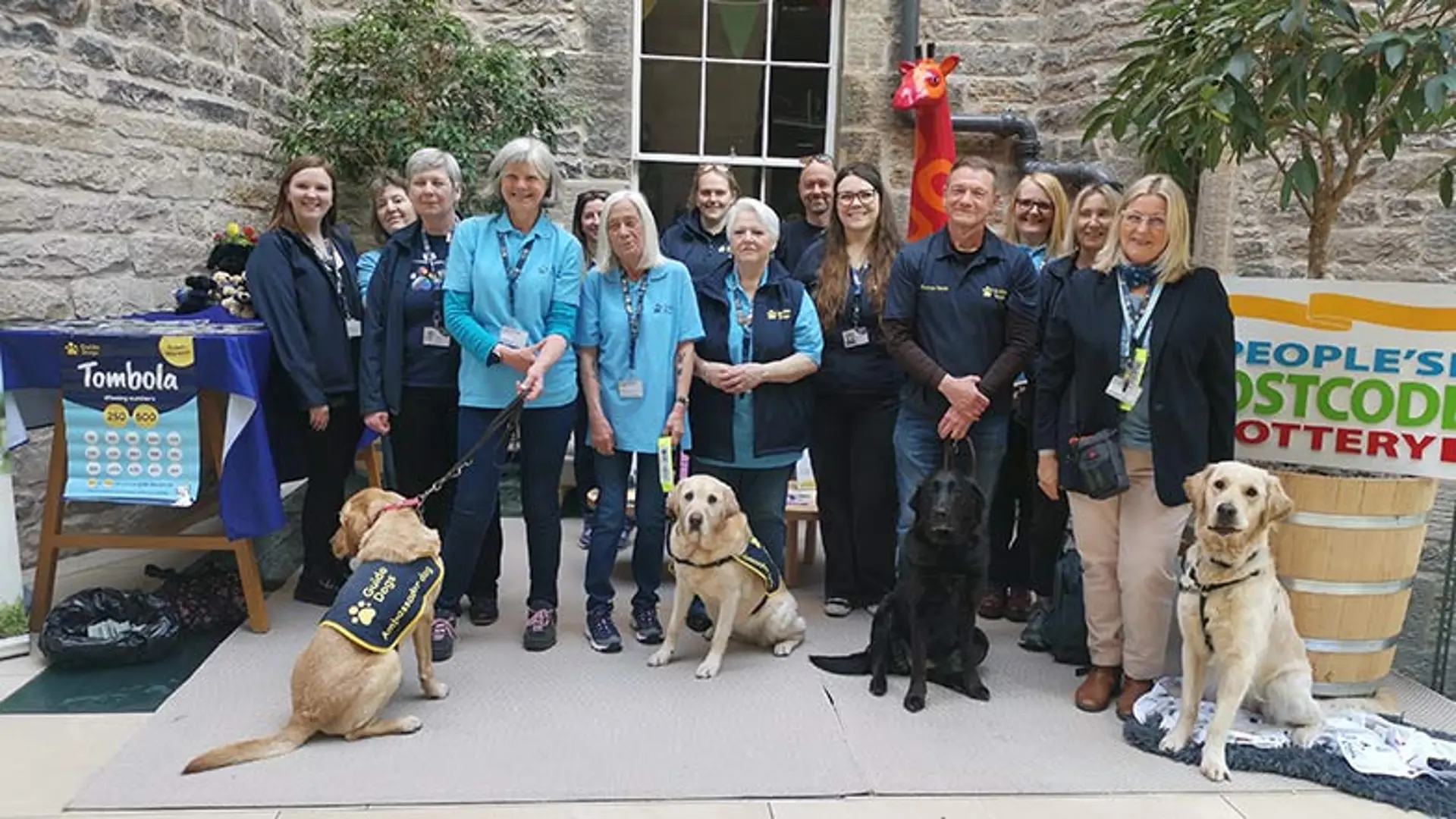 Guide Dogs staff and dogs in training with postcode lottery staff and posters