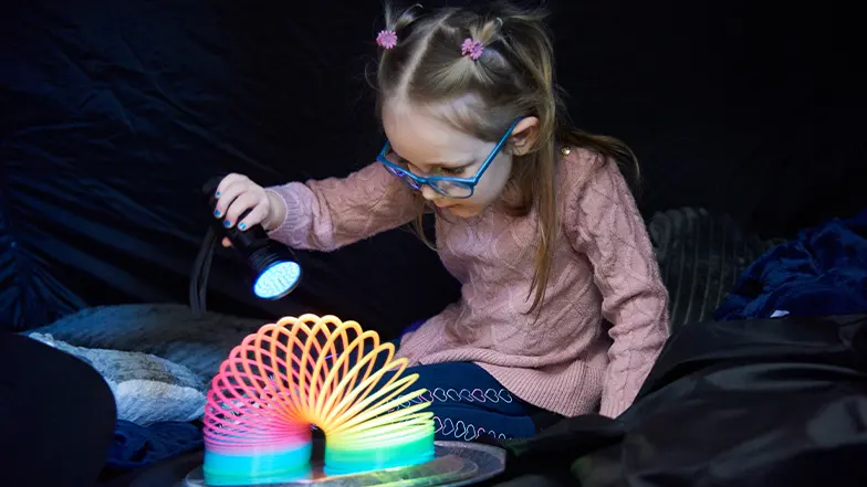 A young girl with a vision impairment plays with a torch and a colourful slinkie as part of sensory play.