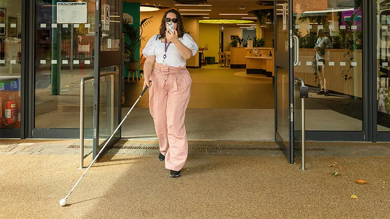 Cerys using a cane and her phone to navigate on the street