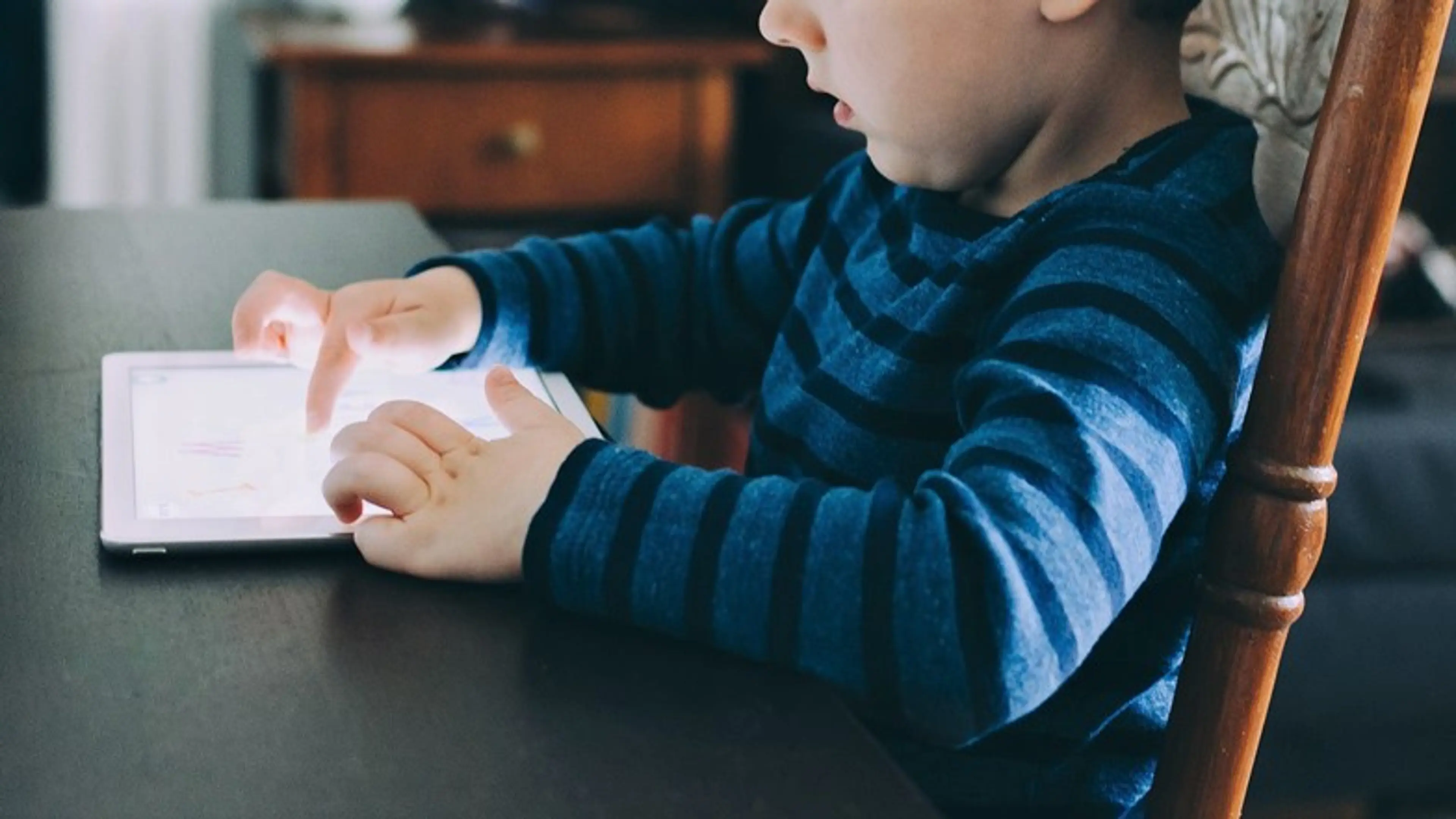A young child using an iPad while sitting at a table
