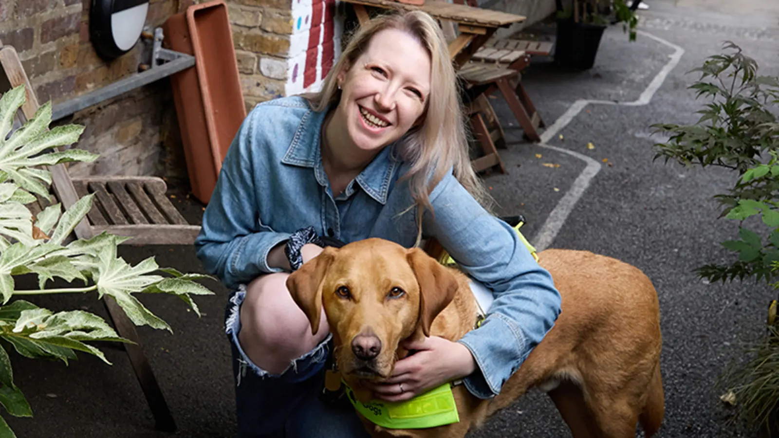 Guide dog owner Emma kneels with her arm around her guide dog Archie. They both look to camera and Emma smiles.