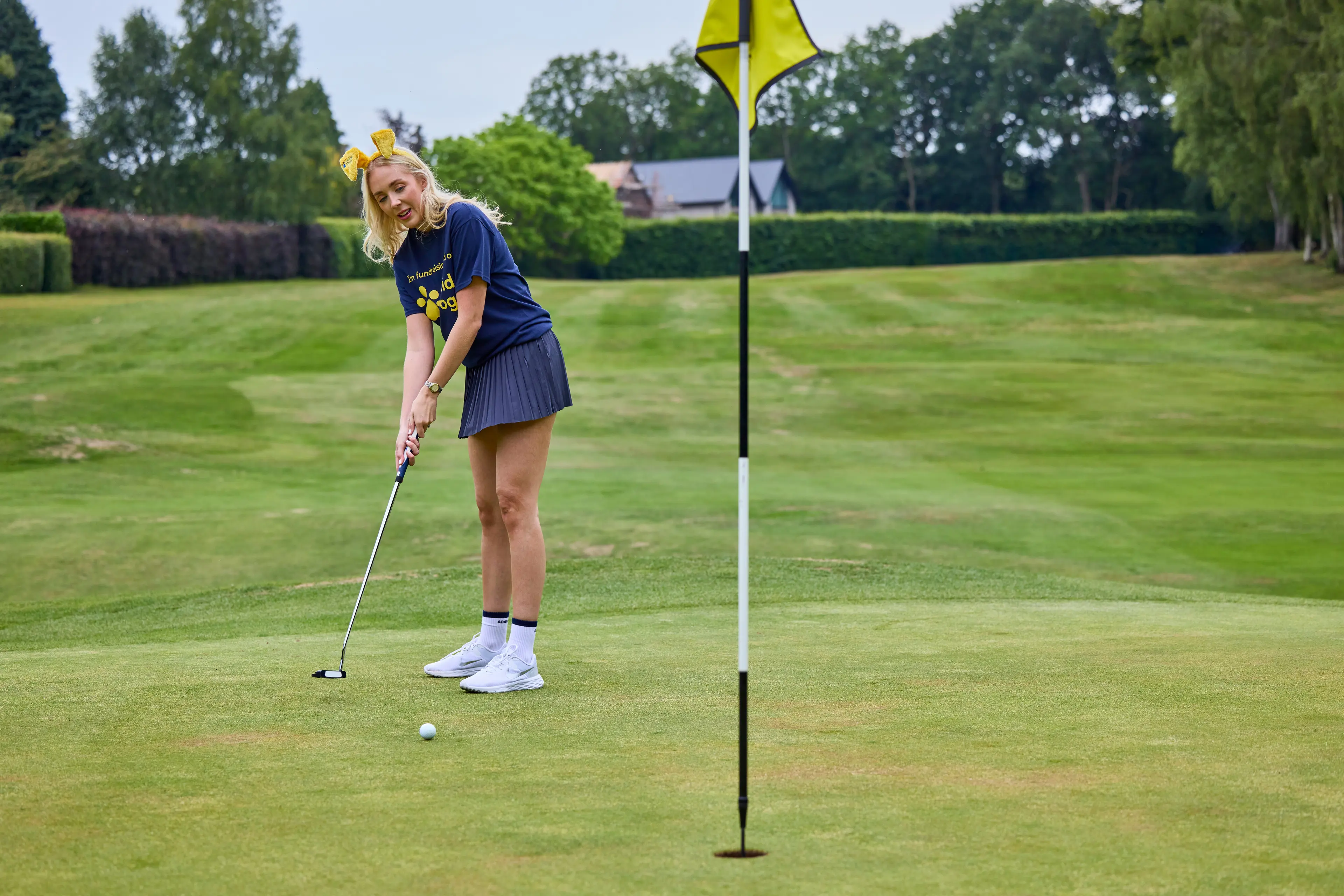 A woman plays golf wearing a Guide Dogs tshirt.