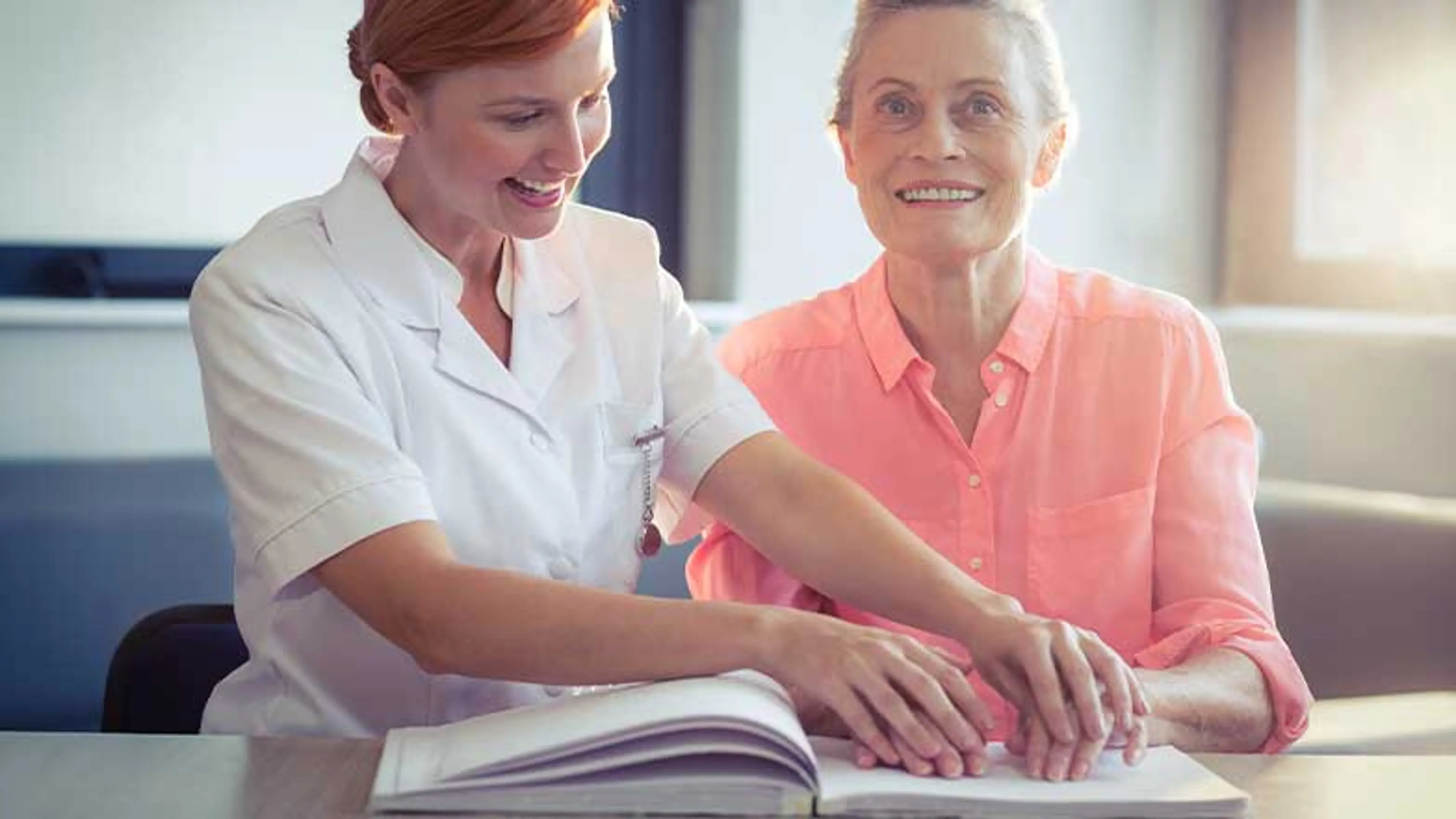 A care worker helping a lady read braille