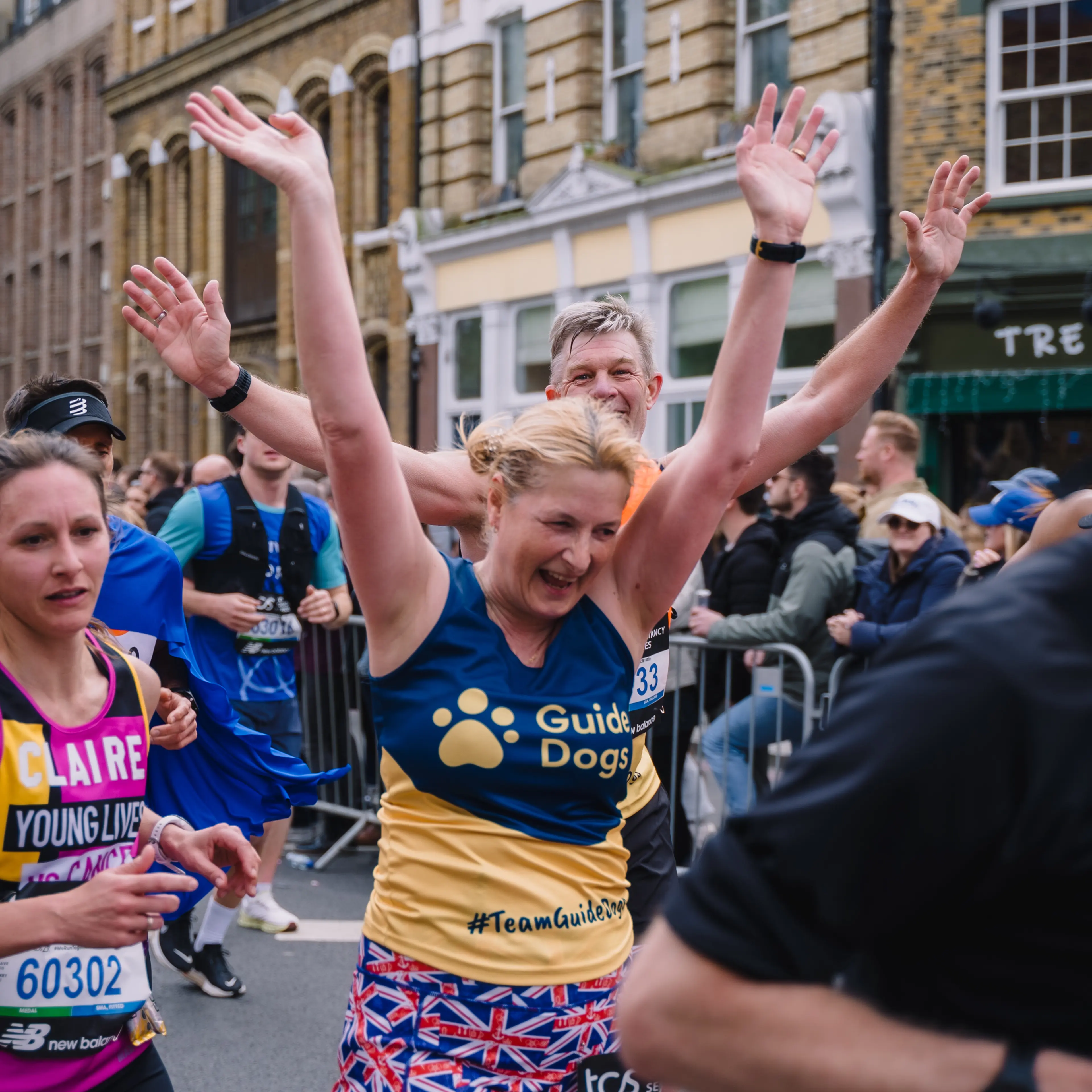 A Guide Dogs runner raises her arms and smiles at the London Marathon.