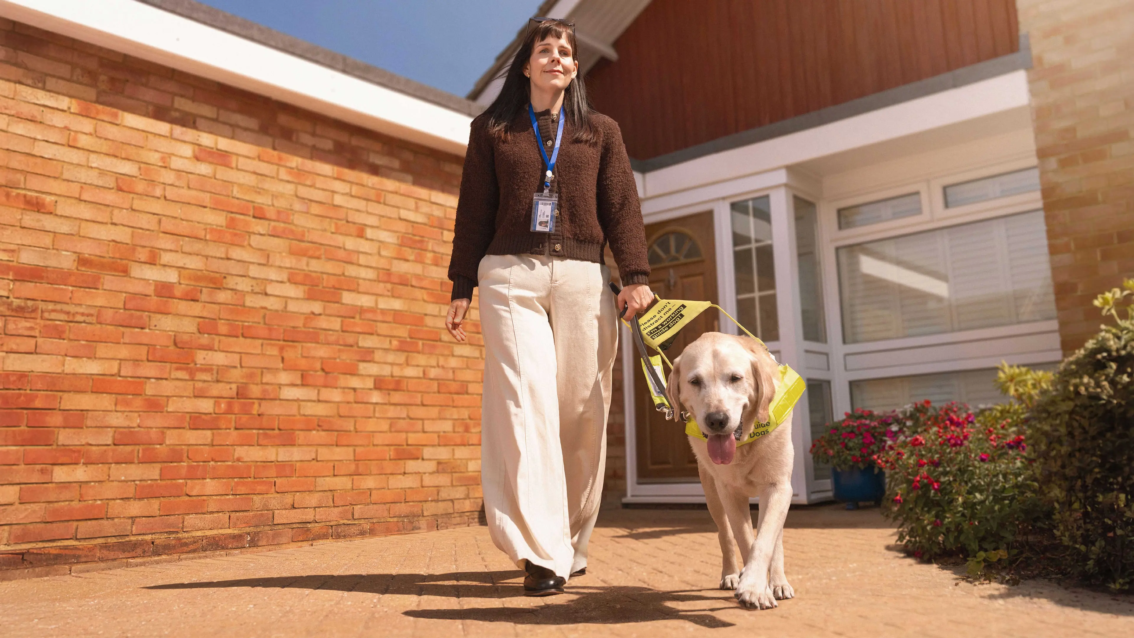 Lorna walks confidently with her guide dog on a sunny day.