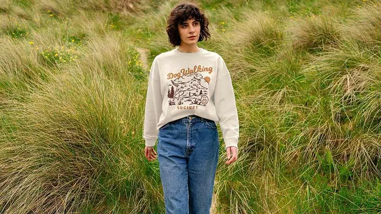 A woman standing in field wearing a sweatshirt from the Guide Dogs Teemill store
