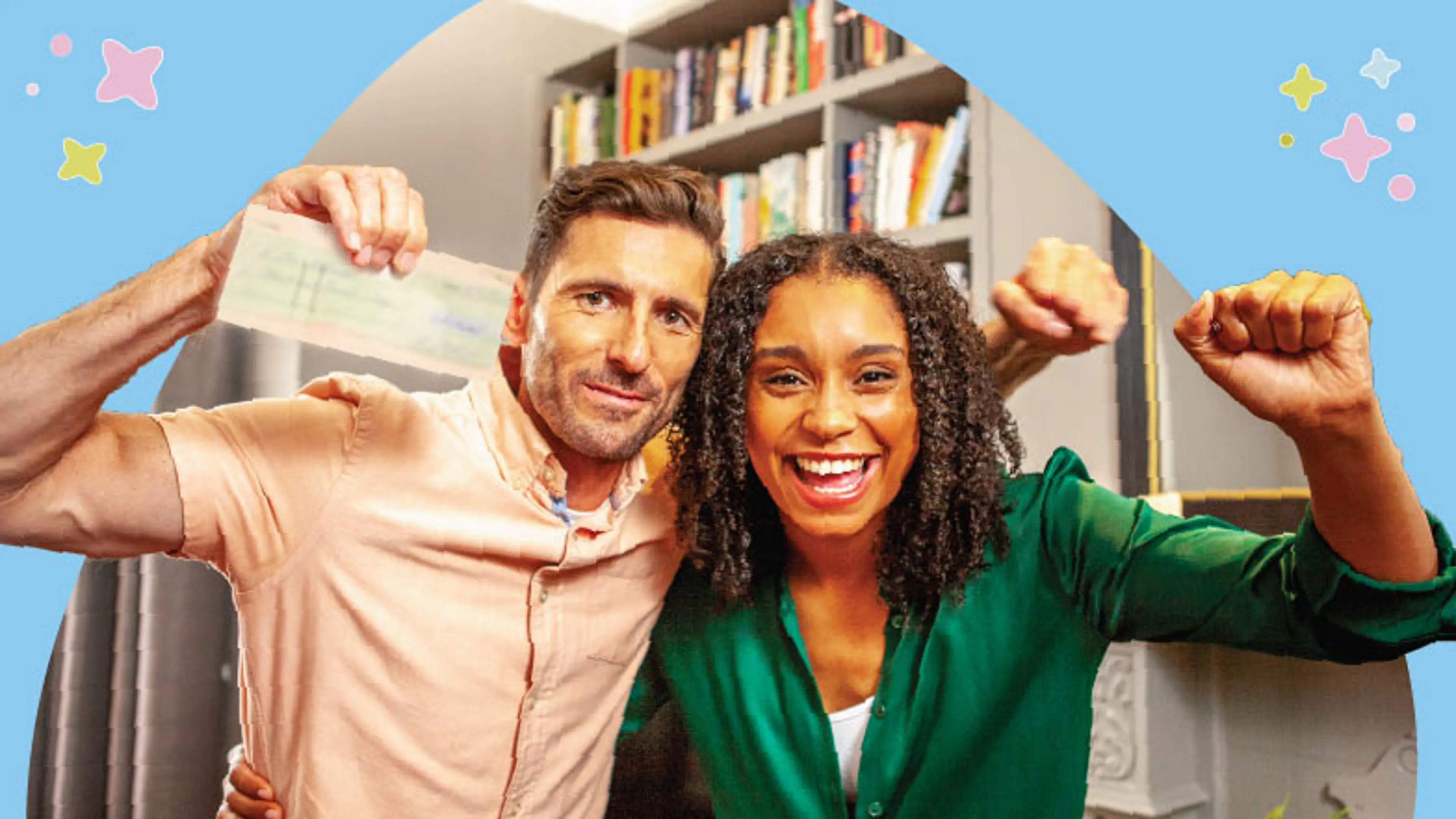 A man and woman stand together raising their fists in celebration, the man is holding a cheque.