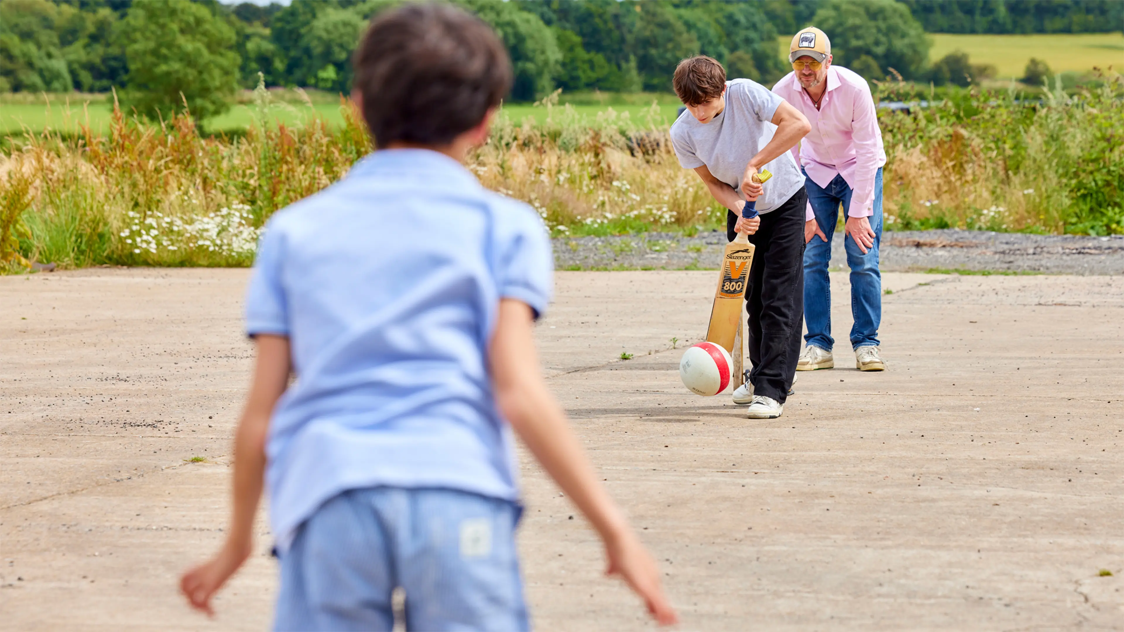 An action shot of Archie, who has a vision impairment, as he hits a cricket ball. He's playing cricket with his brother and Dad. 