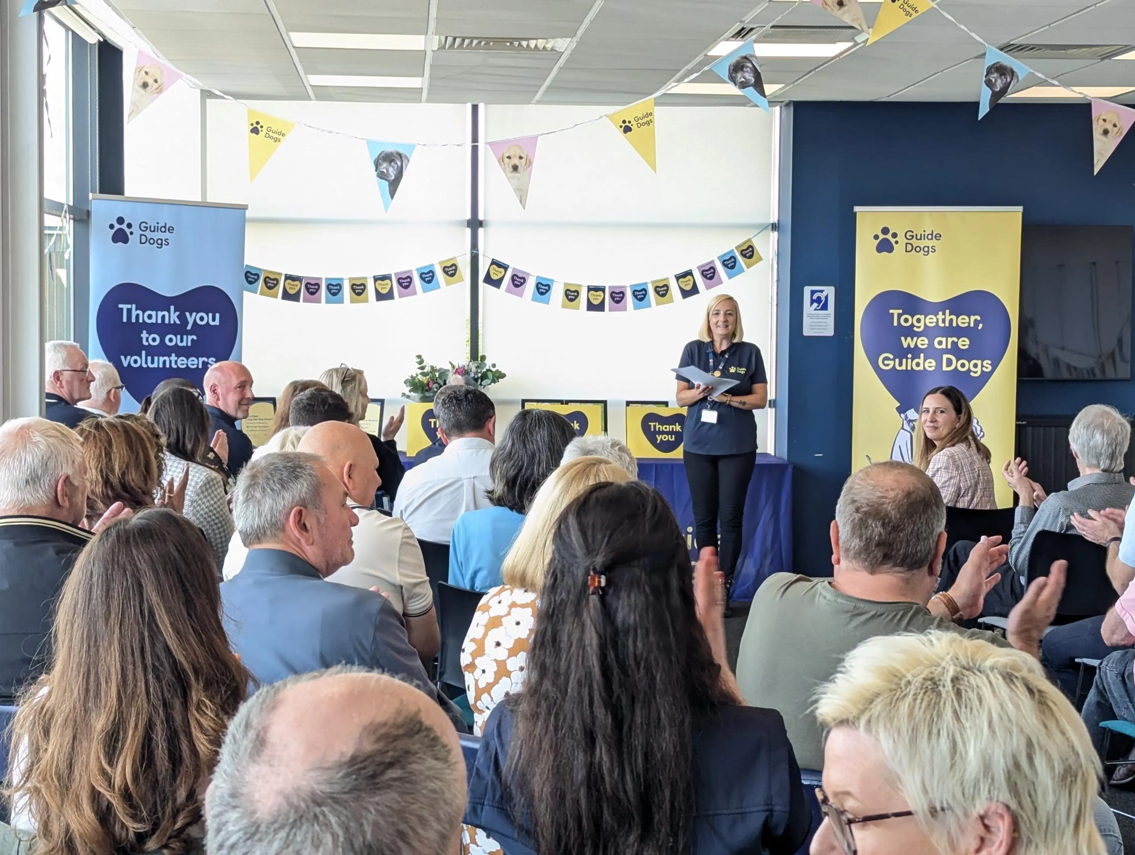 A group of volunteers listen to a member of Guide Dogs staff speaking