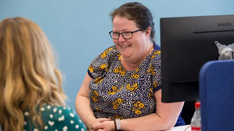 Two guide dogs volunteers working in an office. One is facing the camera smiling.