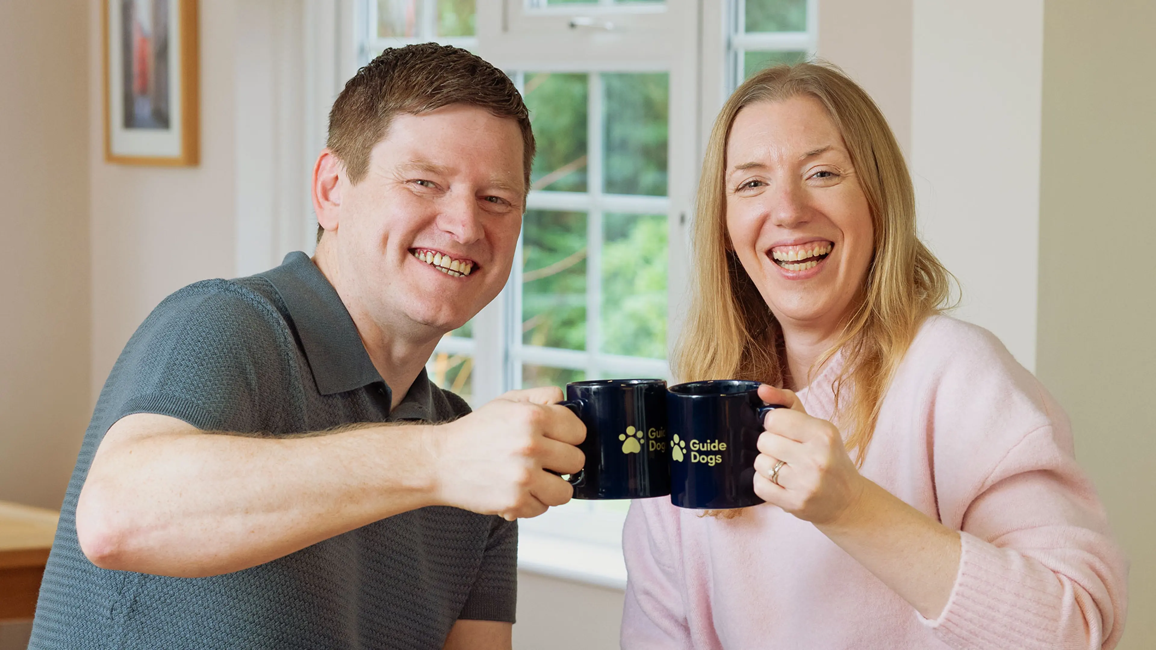 Smiling sponsor a puppy sponsors Kim and Dan clinking Guide Dogs' branded mugs.