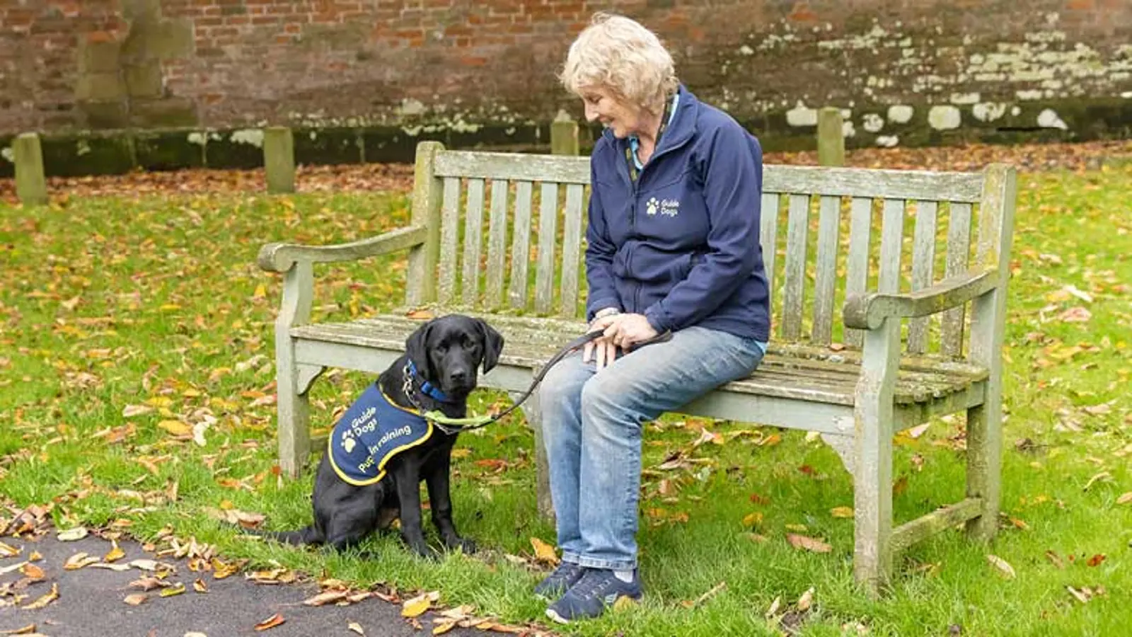 Puppy Raiser Andreina sitting on a bench looking at Jack beside her wearing his puppy coat.
