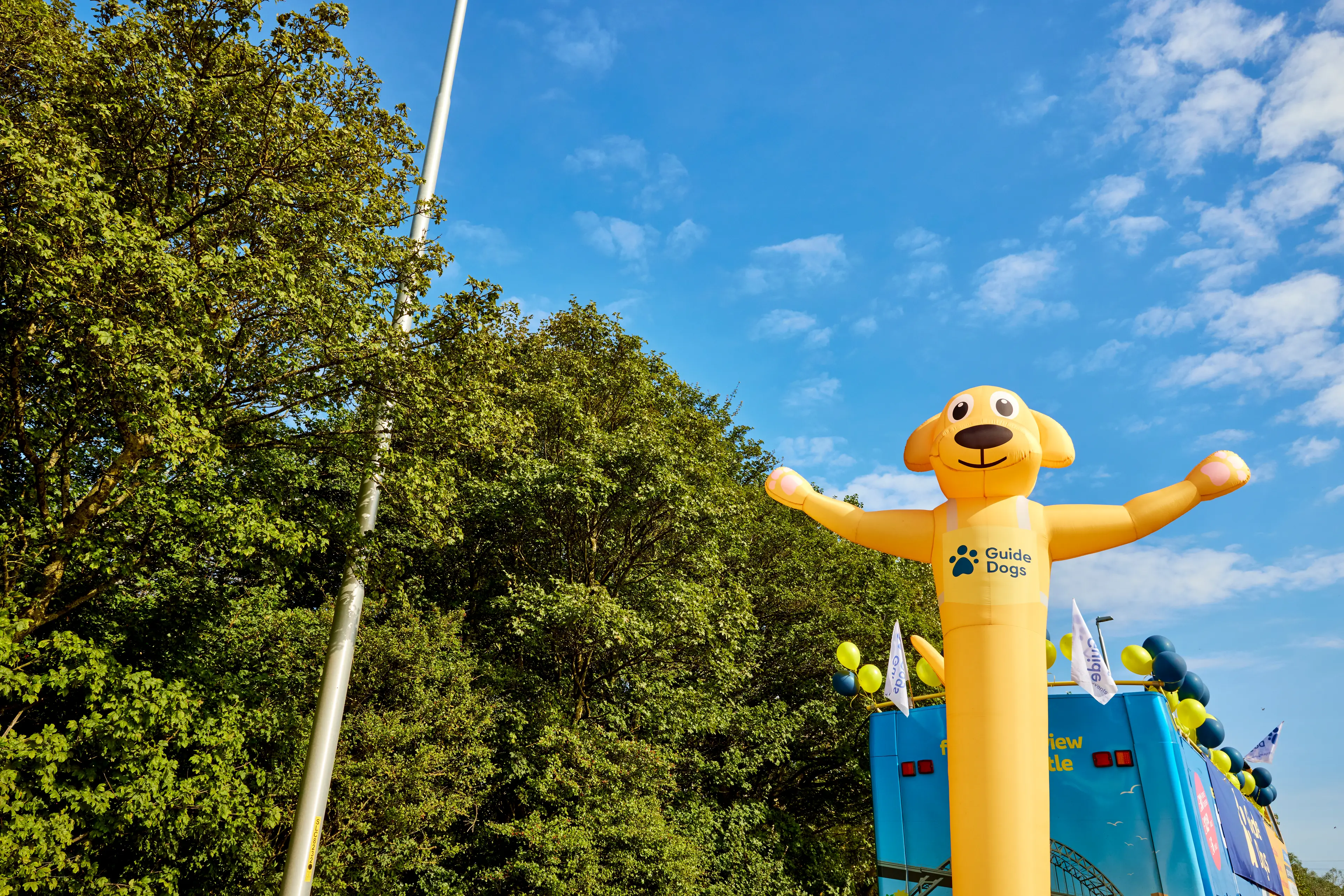 A large inflatable tube man shaped like a golden labrador with the Guide Dogs logo against trees.