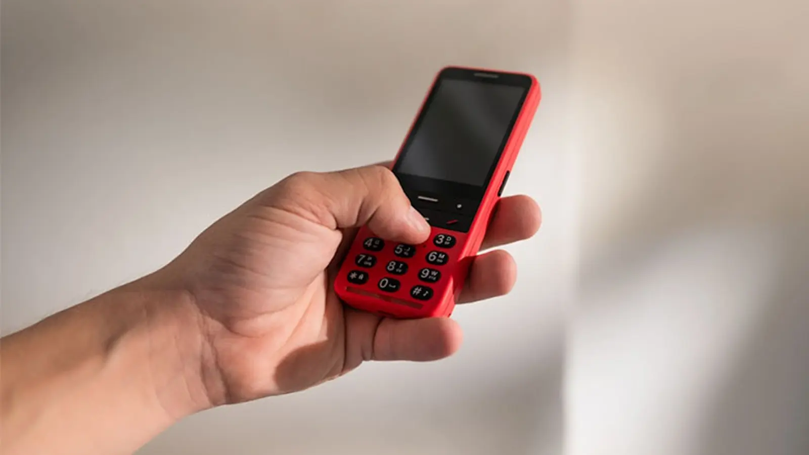 A person holding a red Blindshell classic mobile phone in their hand