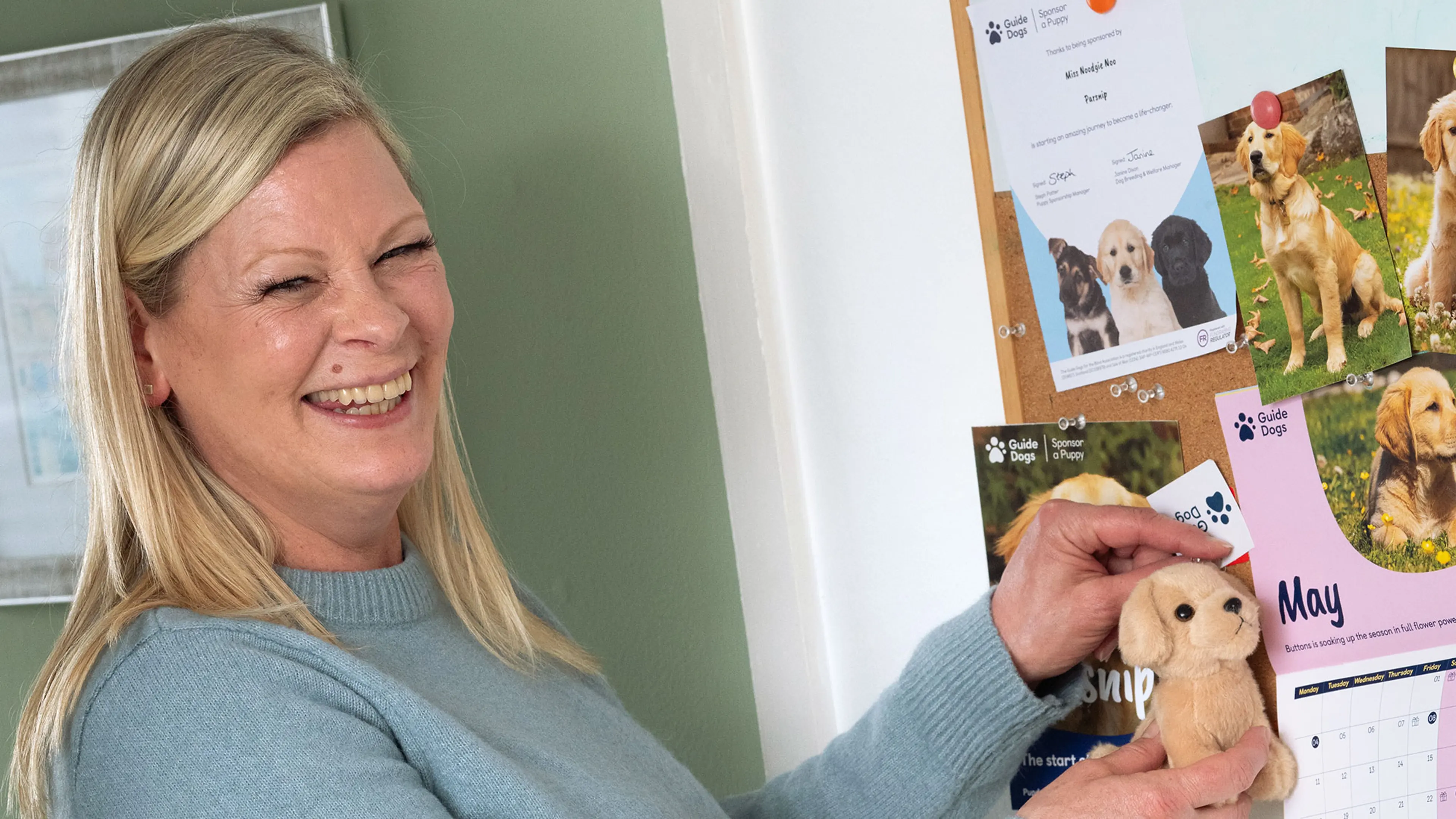 Lindsay smiling whilst she pins a picture of her sponsored pup on her kitchen note board.