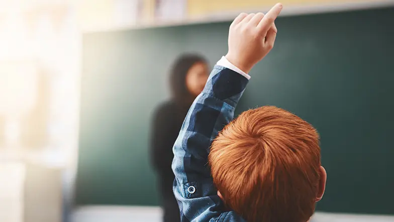 A boy putting his hand up in class.