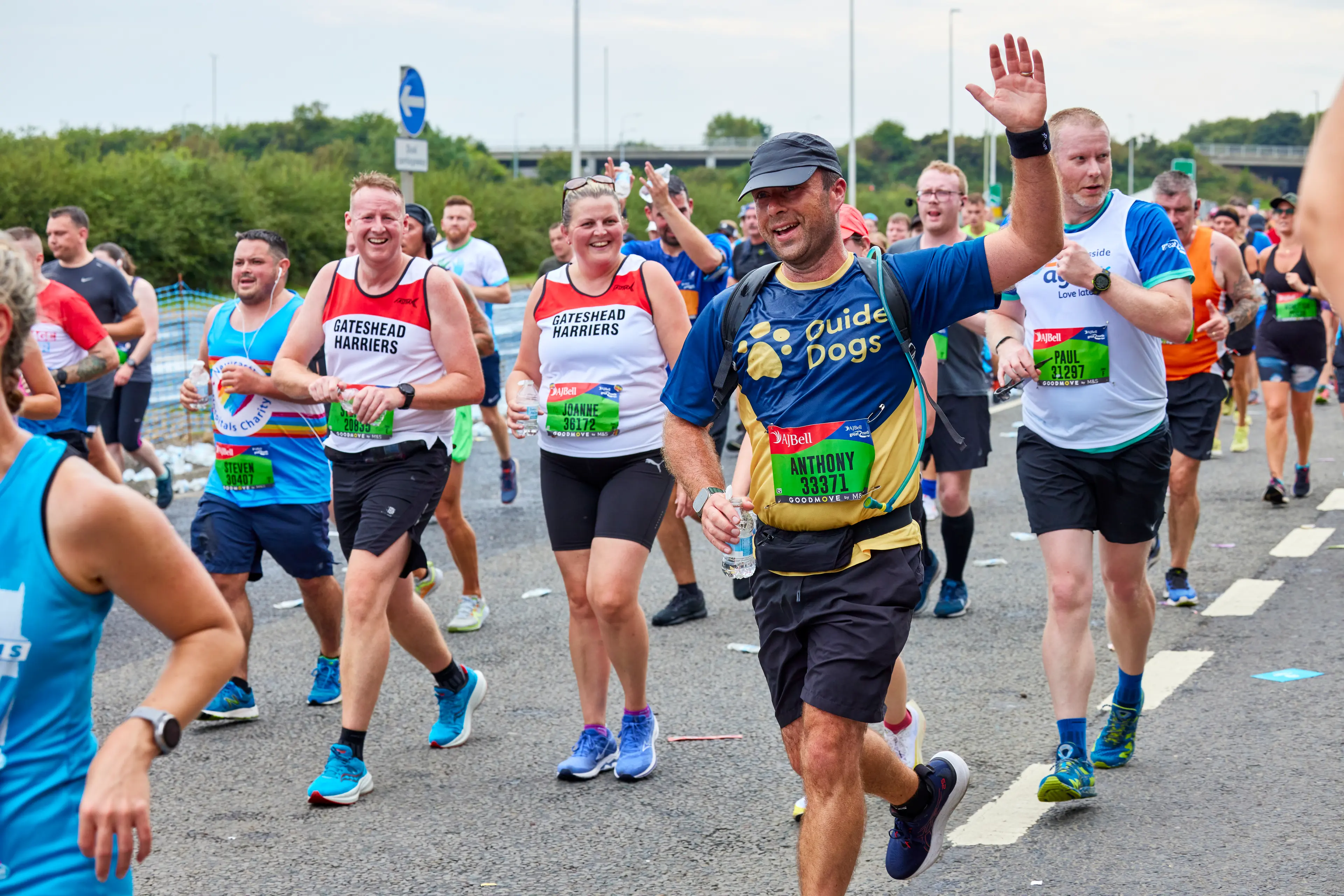A runner for Guide Dogs waves his hand in the air as he passes cheering supporters.