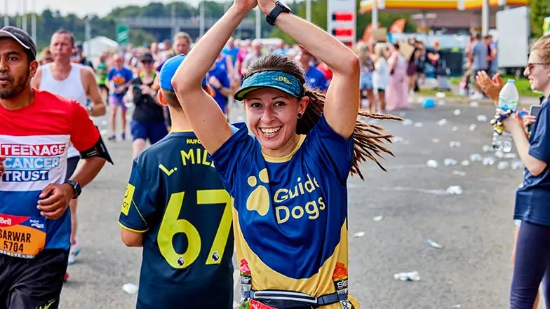 A fundraiser wearing a Guide Dogs t-shirt with their hands in the air running.    