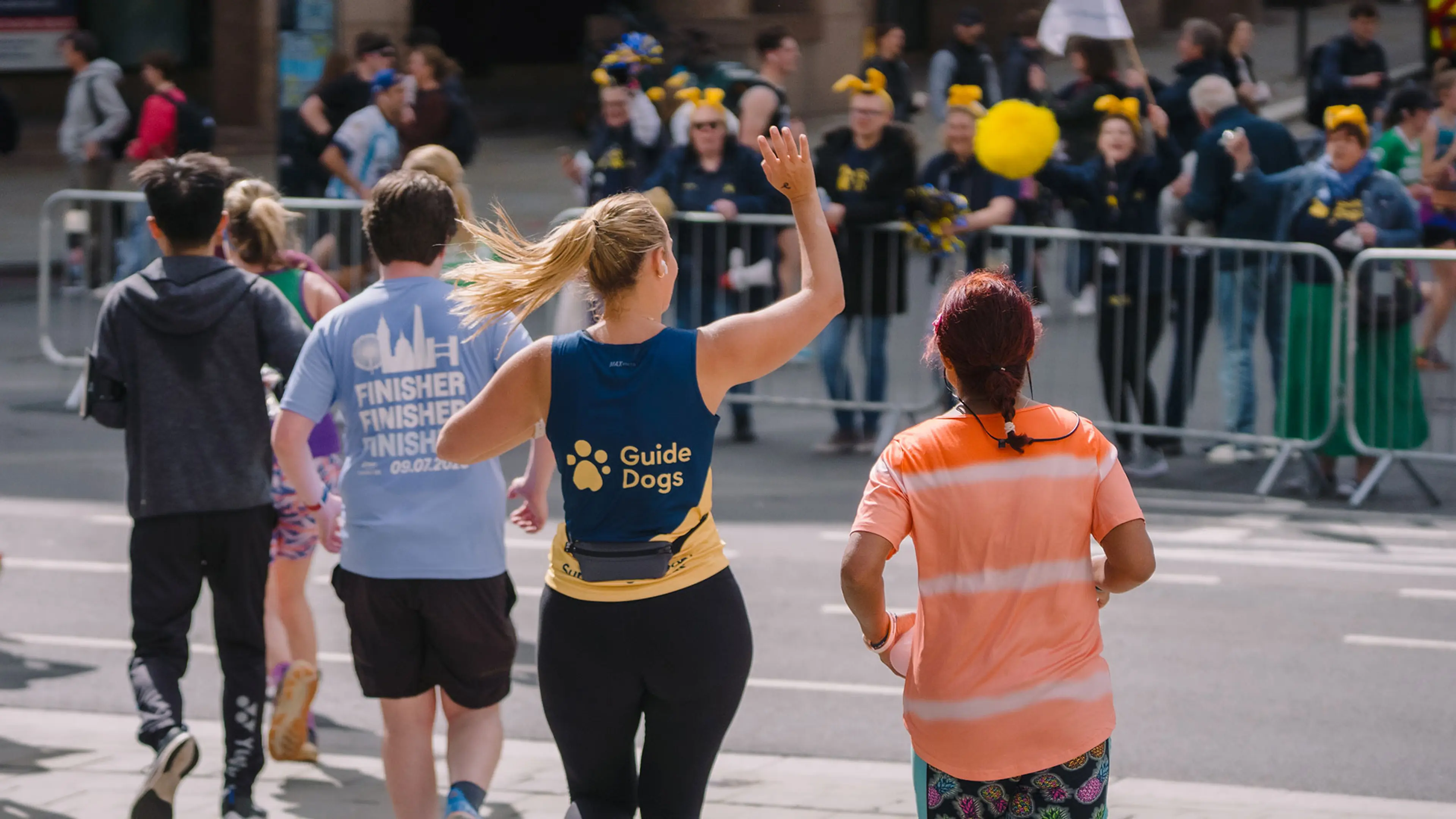 A runner in a Guide Dogs vest waving to the Guide Dogs supporters as she runs by. 