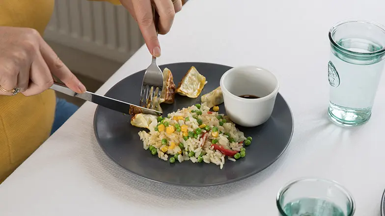 Person cutting into meal at a dining table. The plate is dark to contrast against the white tablecloth