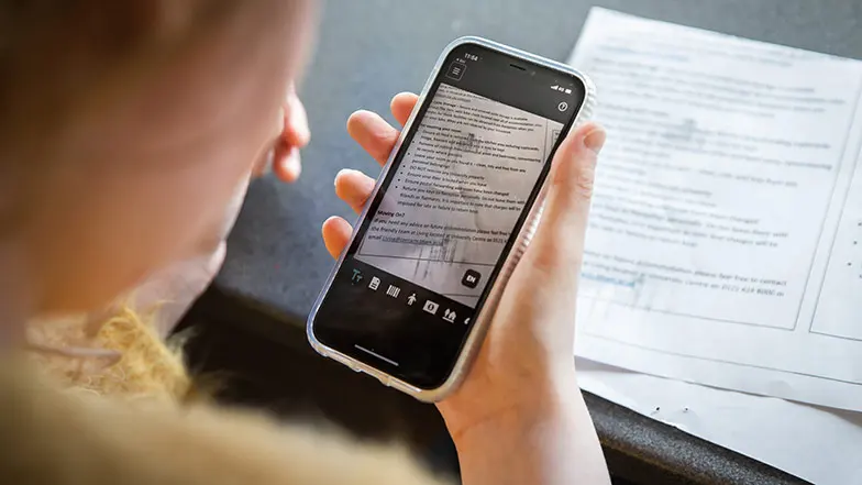 A woman holding an iPhone to a piece of paper with text on to read it with the Seeing AI app