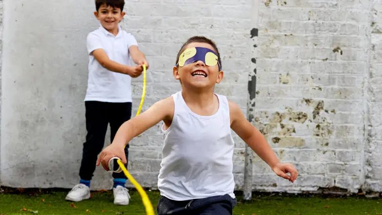 A schoolboy is wearing a Guide Dogs blindfold and completing a race with a guide rope.
