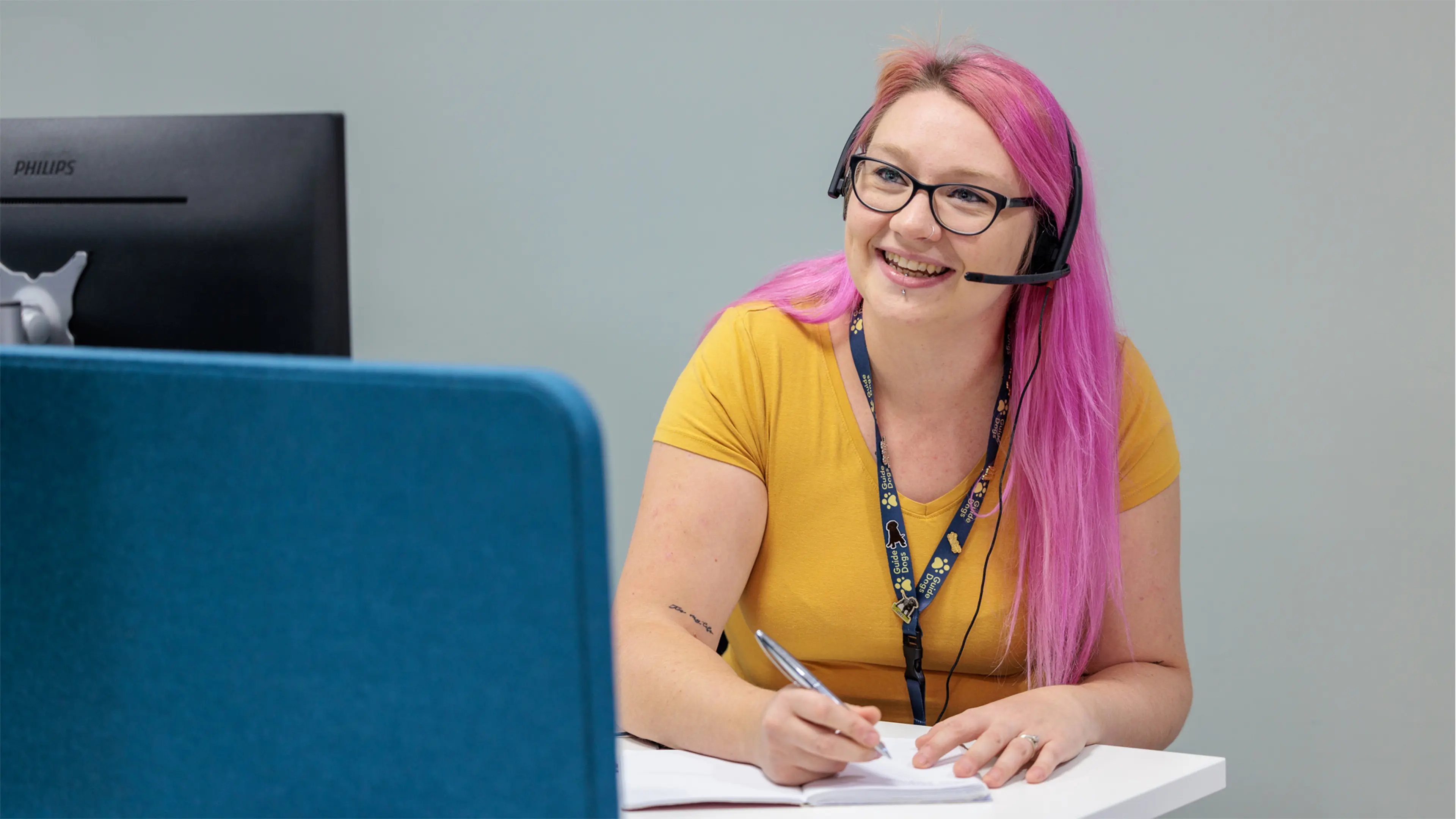A Guide Dogs fundraising team member takes a call on her headset, as she takes notes at her desk.