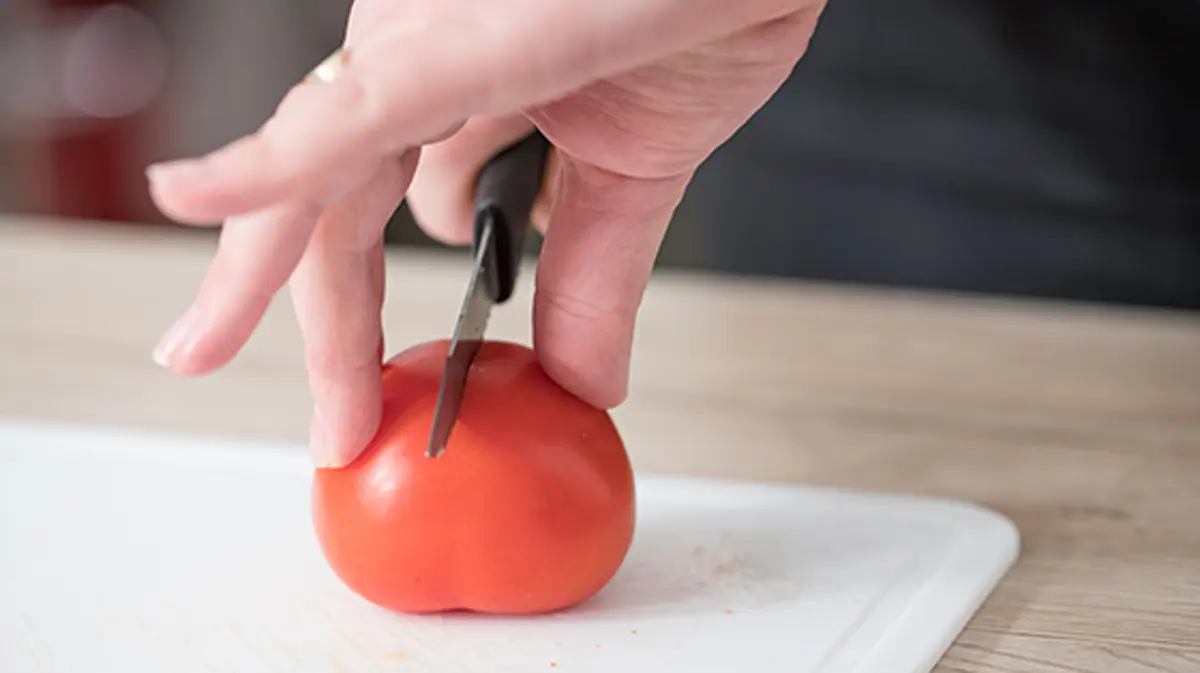 A person chopping a tomato using the bridge technique. 