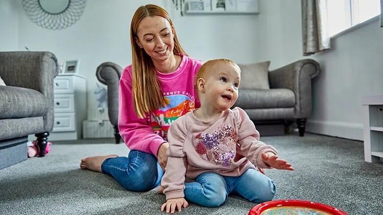 Eliza sits with her mum Lauren, in their living room. They're both smiling.