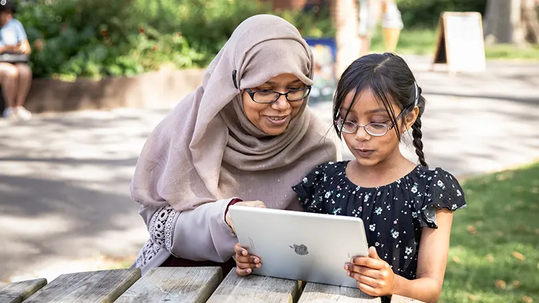 Girl with her mum at a picnic bench looking at an iPad