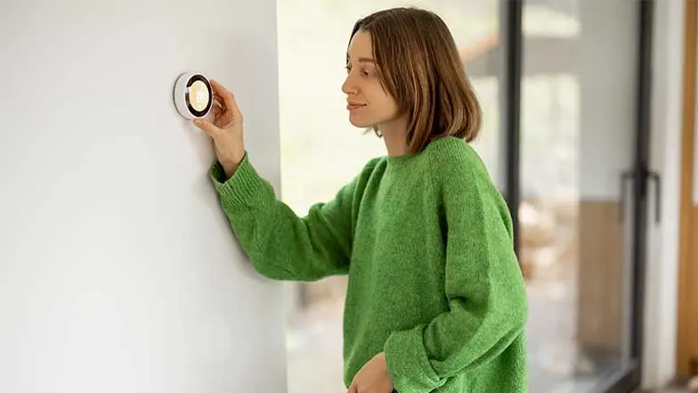 A woman uses a smart thermostat to adjust the room temperature.