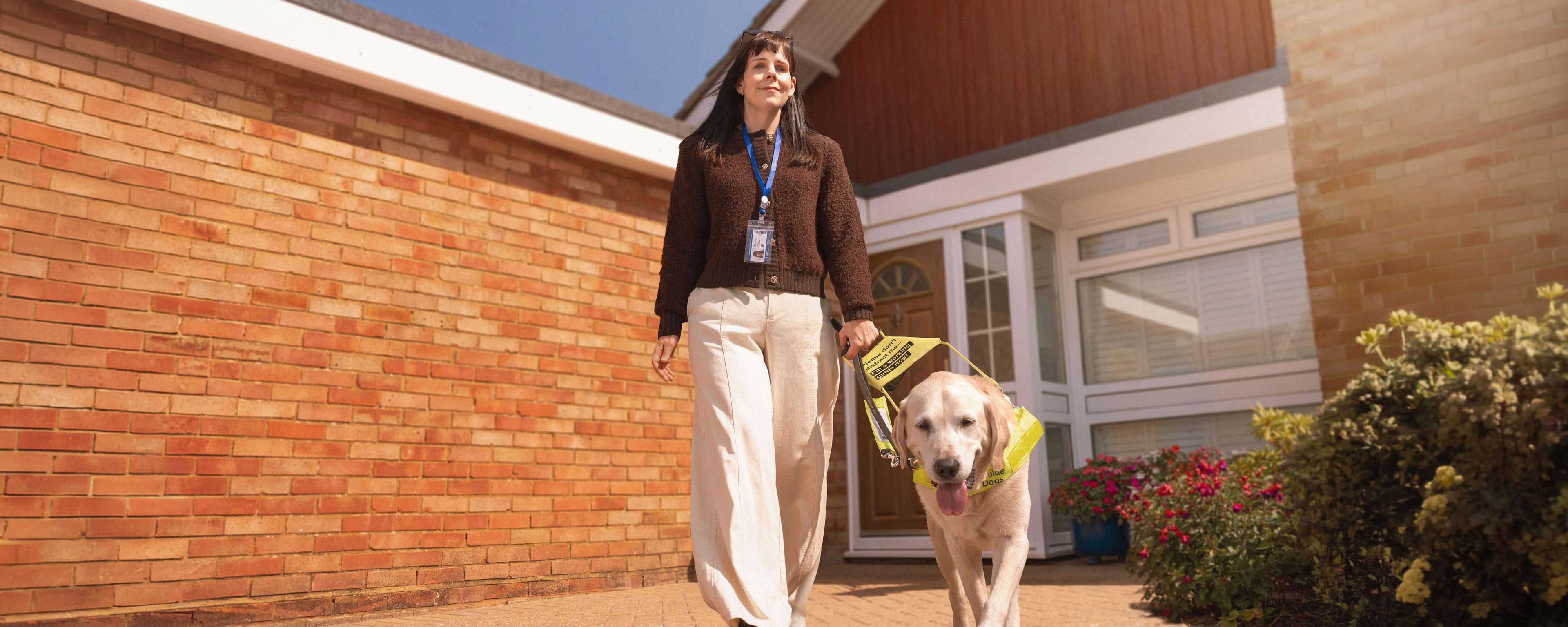 Lorna walks confidently with her guide dog on a sunny day.