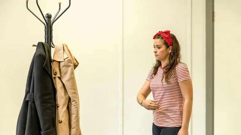 A woman demonstrates lower body protection techniques next to a coatstand.