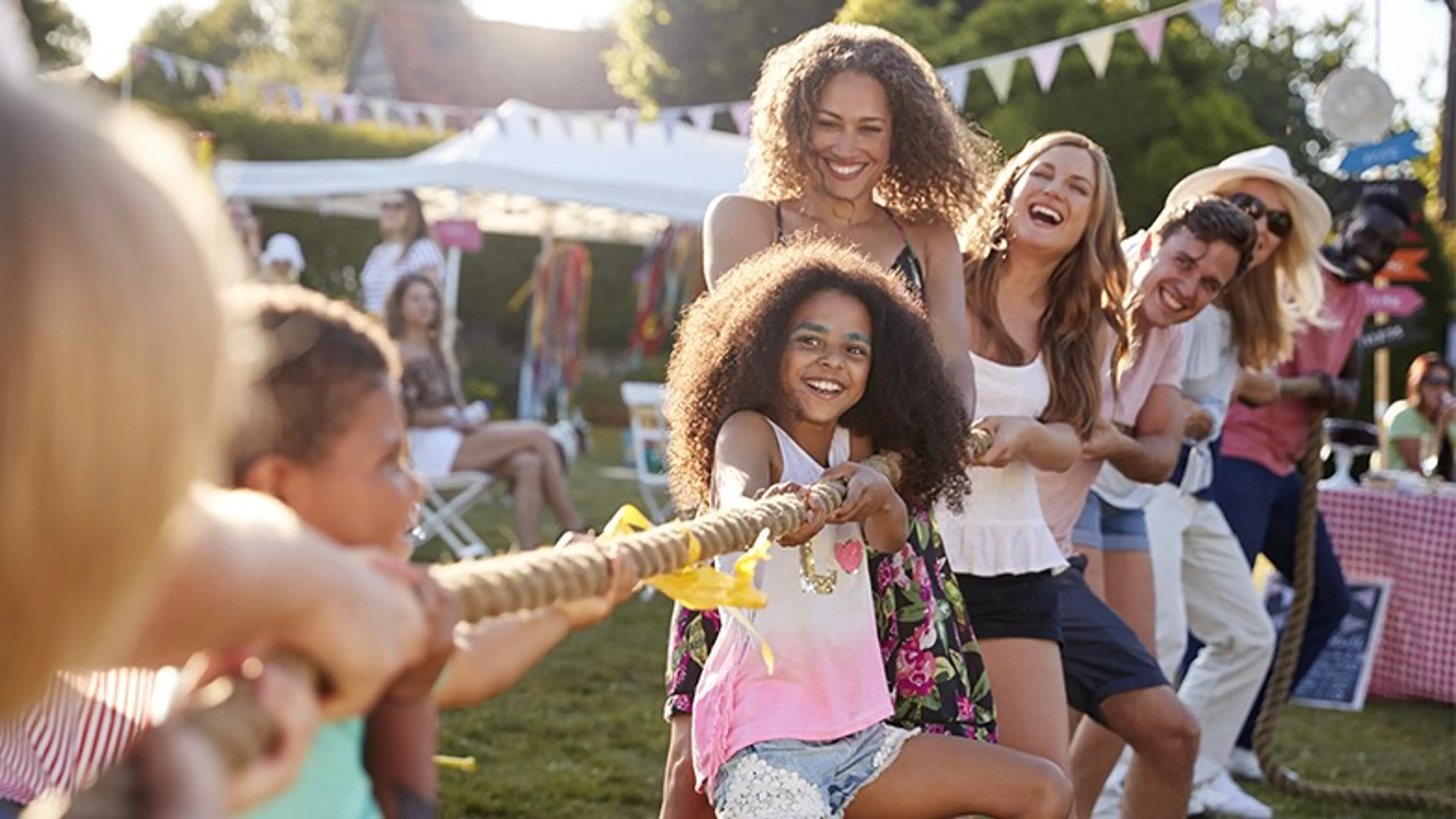 A group of people smiling playing tug of war in an outdoor setting