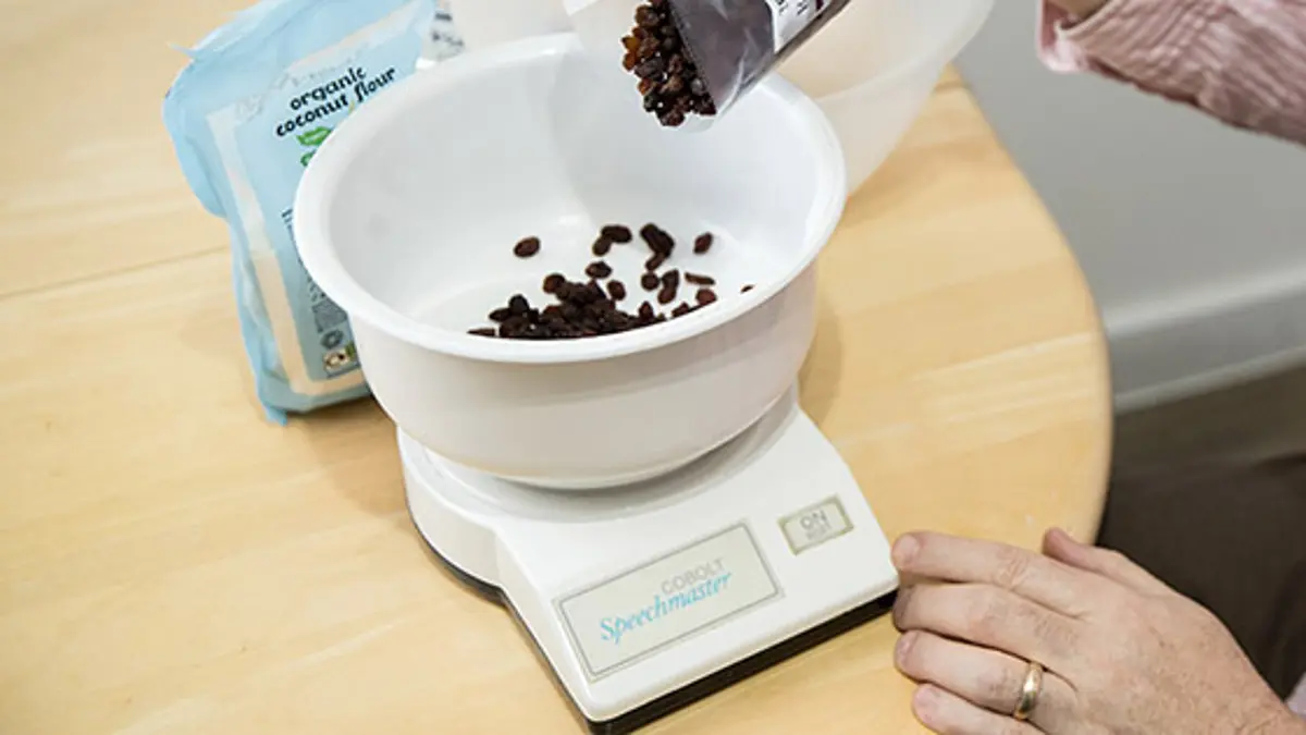A person pouring raisins into a set of talking scales.