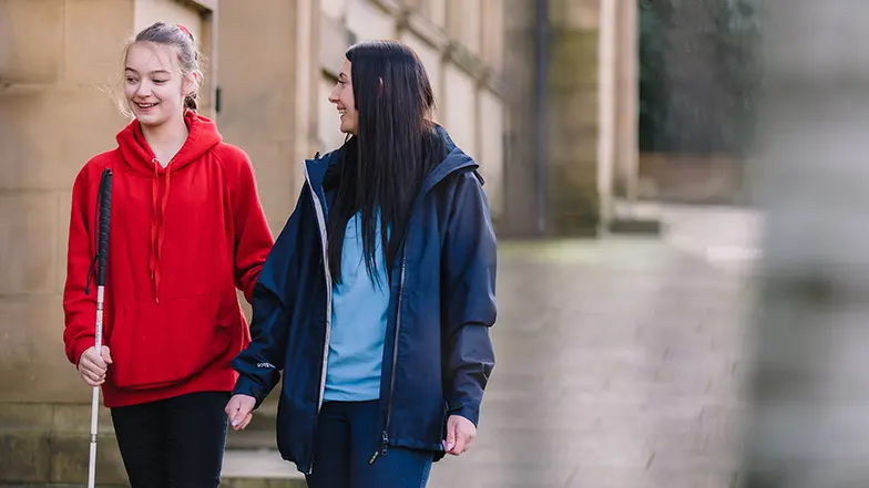 Mia walking outside with long cane and Guide Dogs habiliation specialist