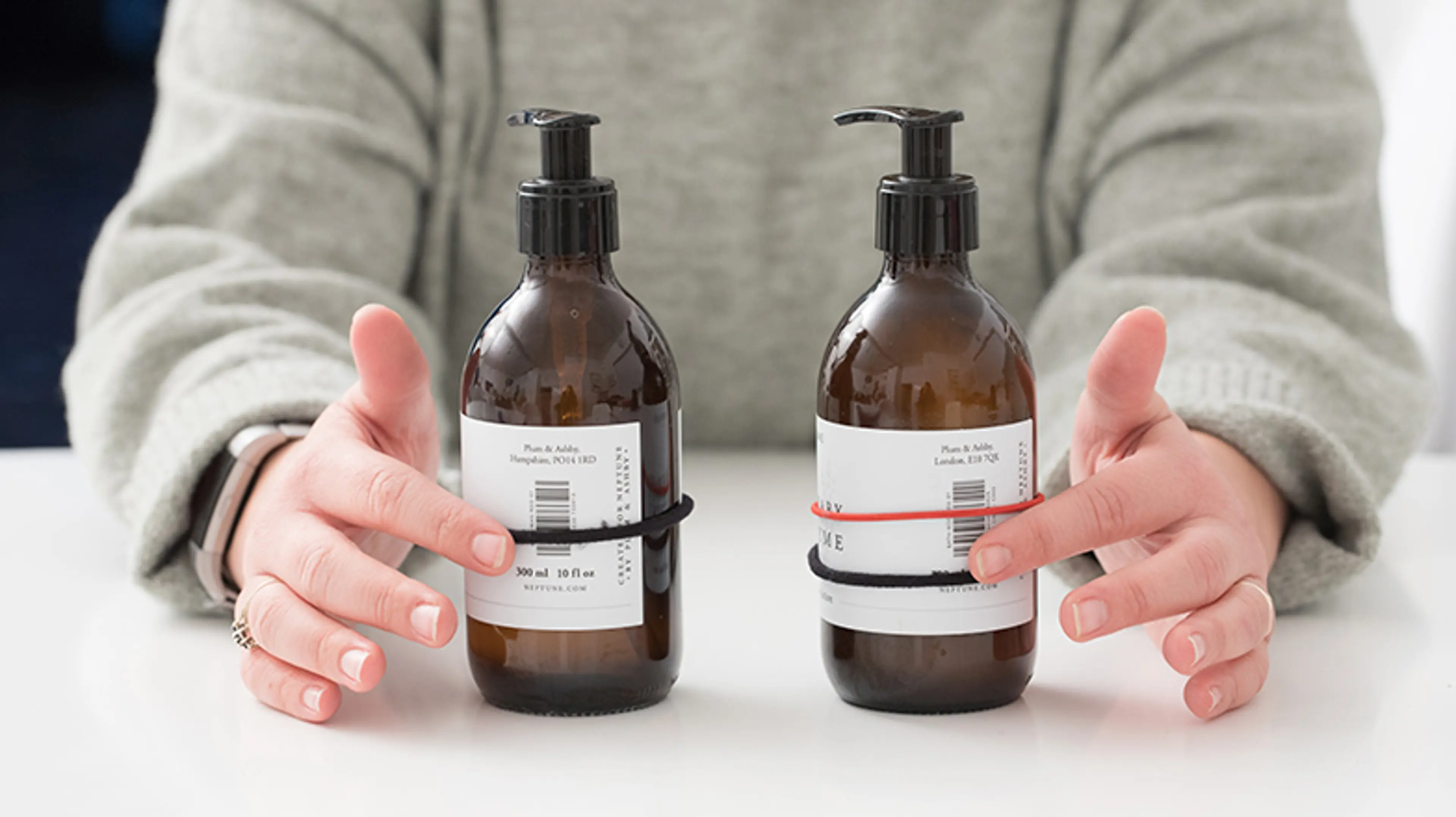 Person pointing at two bottles, one with one elastic band around it, and the other with two