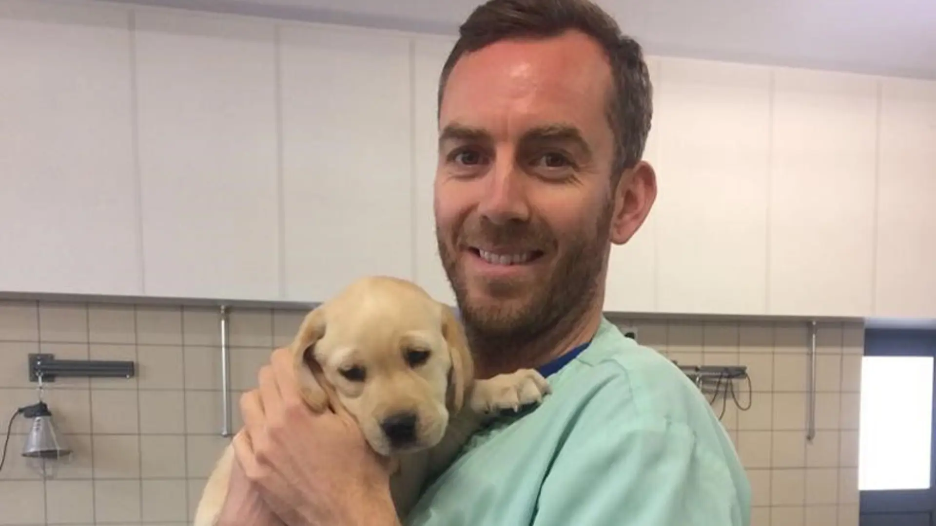 Barry, a Guide Dog Mobility Specialist, holds a puppy and smiles to the camera.