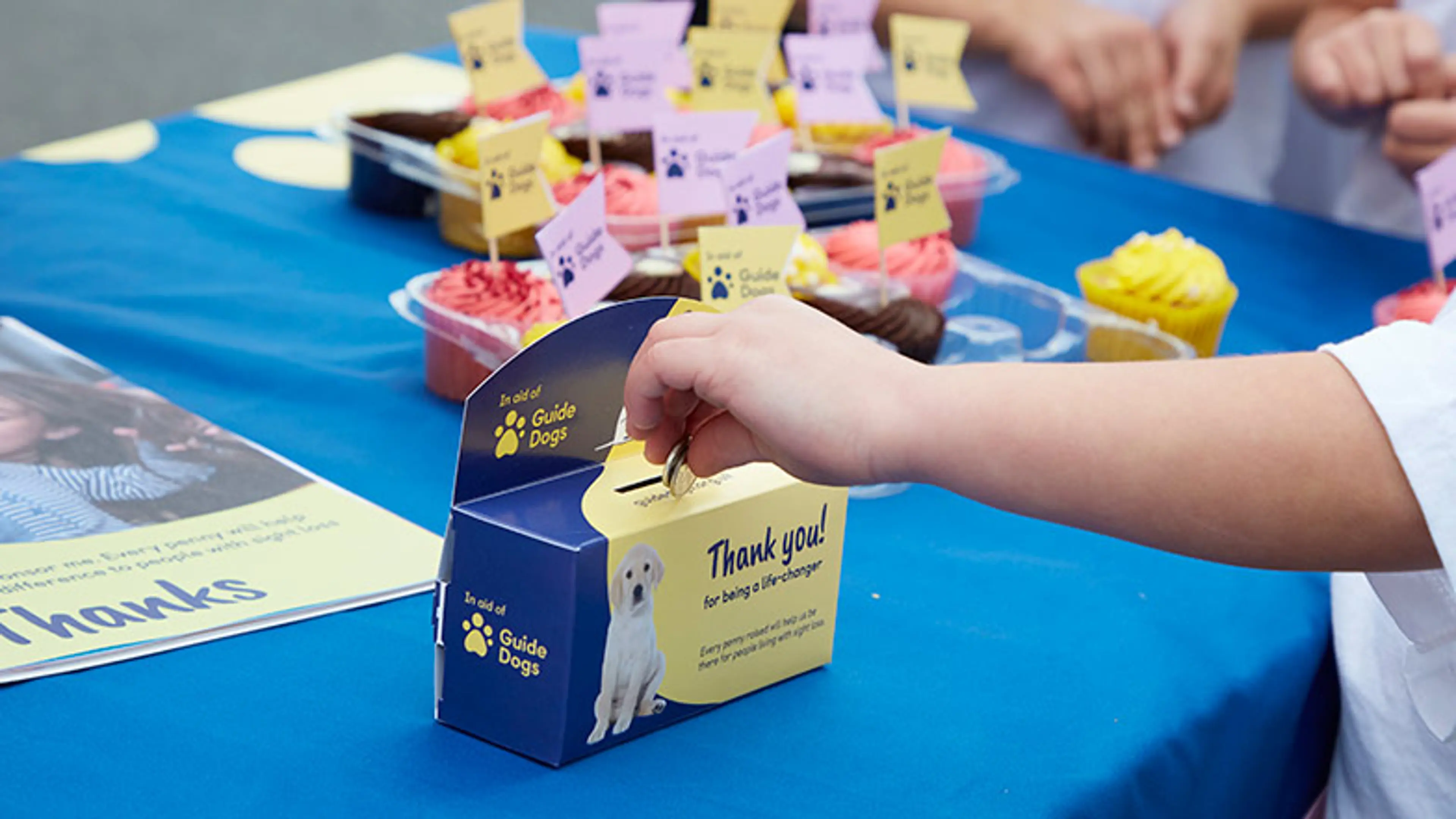 A child puts two 5p into a Guide Dogs coin collector.