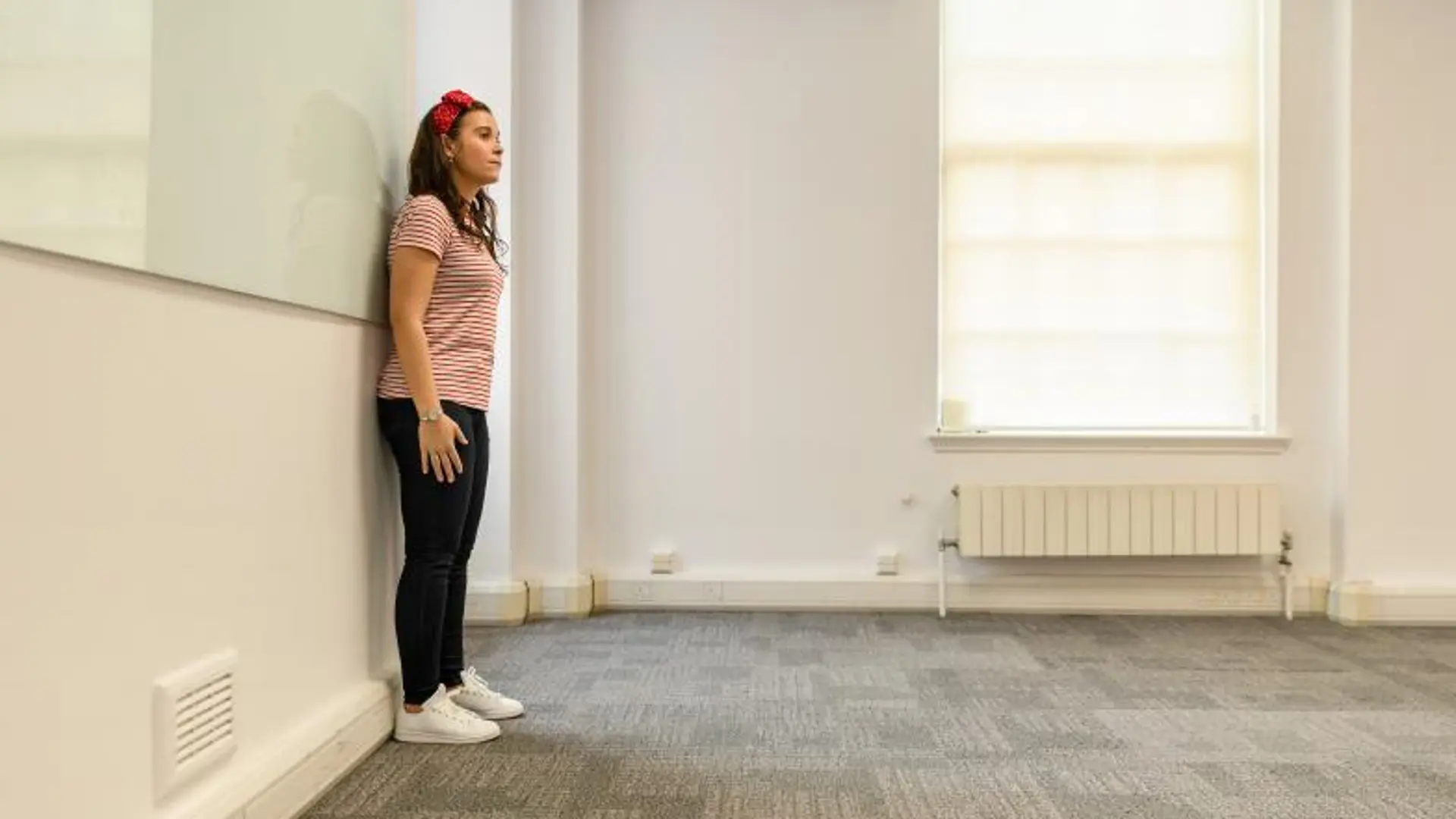 A woman stands against a wall in a meeting room, demonstrating the squaring off technique.